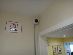 Security camera installation in Cerritos showing camera mounted near exit sign with conduit piping for protected wiring