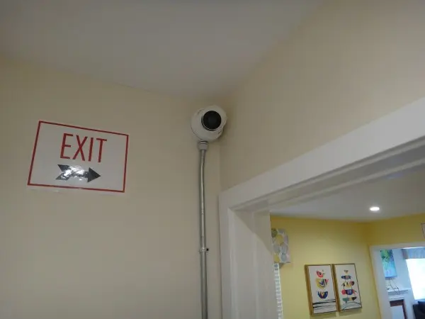 Security camera installation in Cerritos showing camera mounted near exit sign with conduit piping for protected wiring