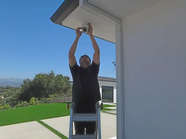 Technician adjusting security camera on ladder to improve coverage and eliminate blind spots