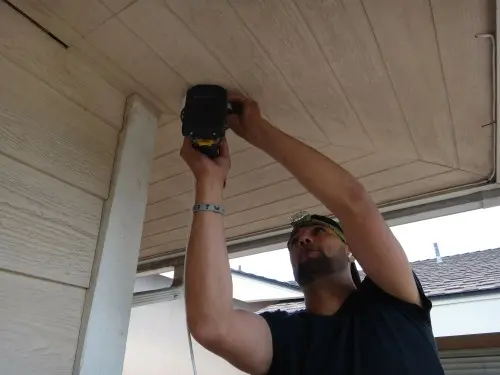 Installer securing outdoor security camera mounting base under roof soffit during residential CCTV installation