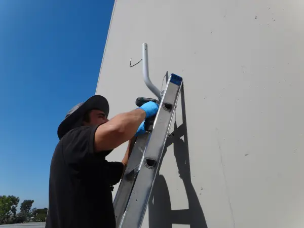 Technician installing a Ubiquiti wireless bridge mounting bracket on a commercial building in Commerce CA as part of a security camera network installation.