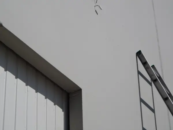 Technician ladder positioned against a commercial building wall near a security camera cable entry point during security camera installation.