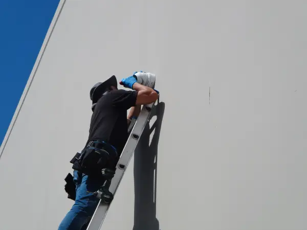 Installer securing a security camera to a commercial building wall during a surveillance system installation.