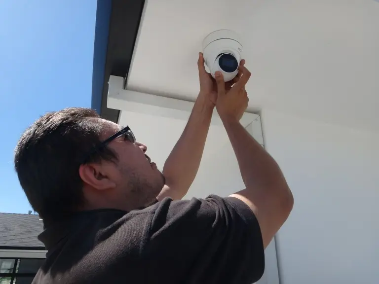Security camera installer mounting and adjusting an outdoor surveillance camera on a residential property