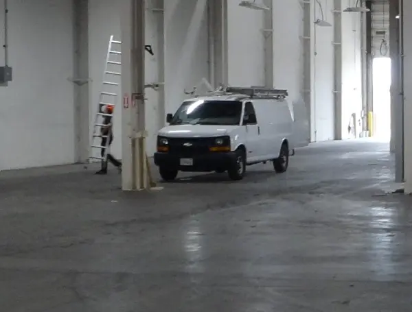 Protection4Less installation van and technician preparing for a commercial security camera installation inside a Paramount warehouse.