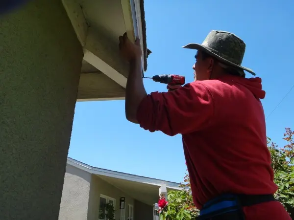 echnician drilling under roof eave for security camera installation in Pico Rivera, CA