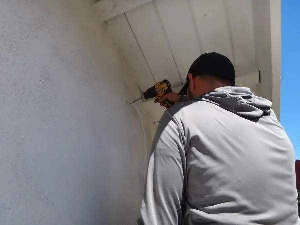Technician drilling to install a security camera junction box at a Fullerton CA home